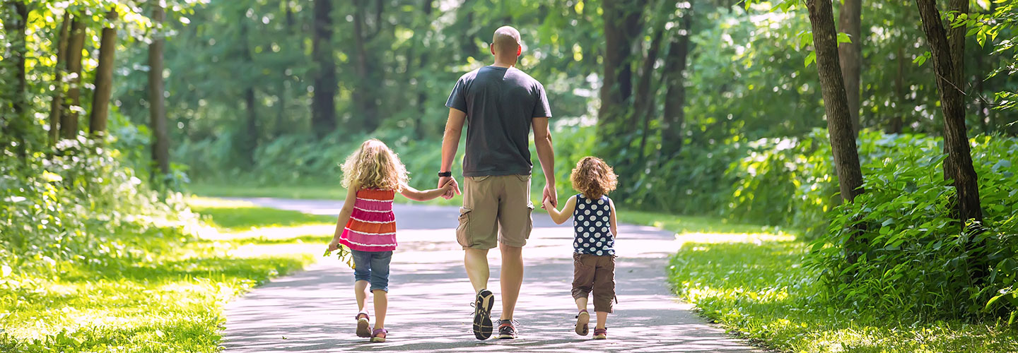 Man walking with two young girls on a park path