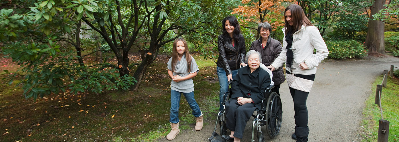 Elderly woman in wheelchair is pushed by three woman and a young girl.